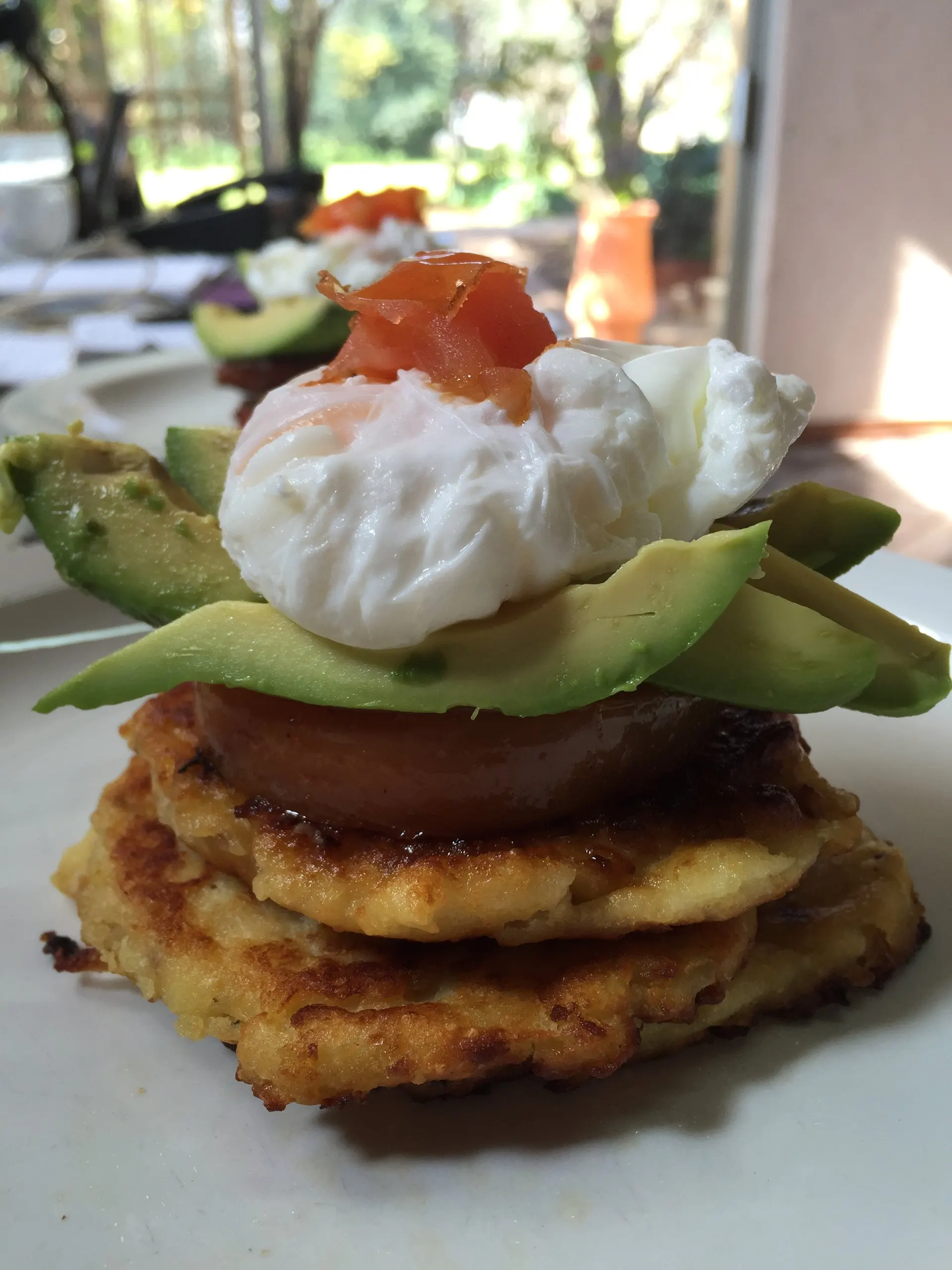 A poached egg, avocado and potato cake stack, breakfast-plated on a terrace