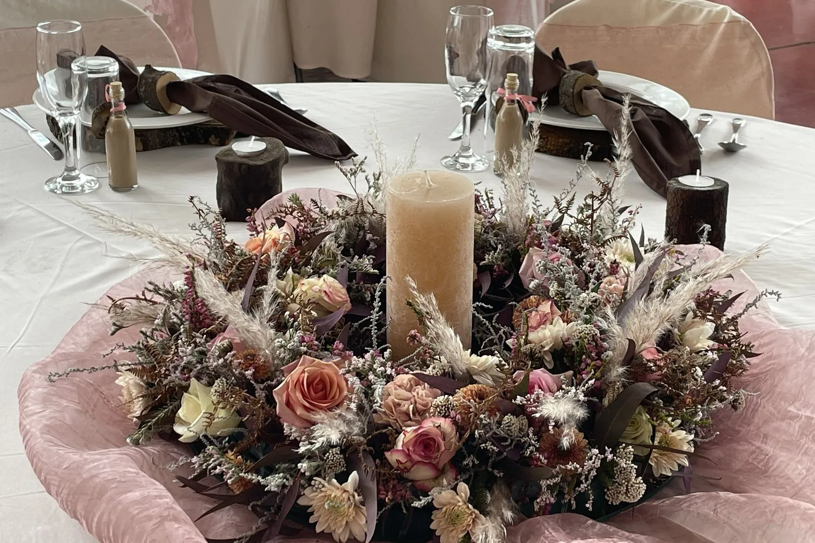 A dried-flower centrepiece with a tall candle on a function table