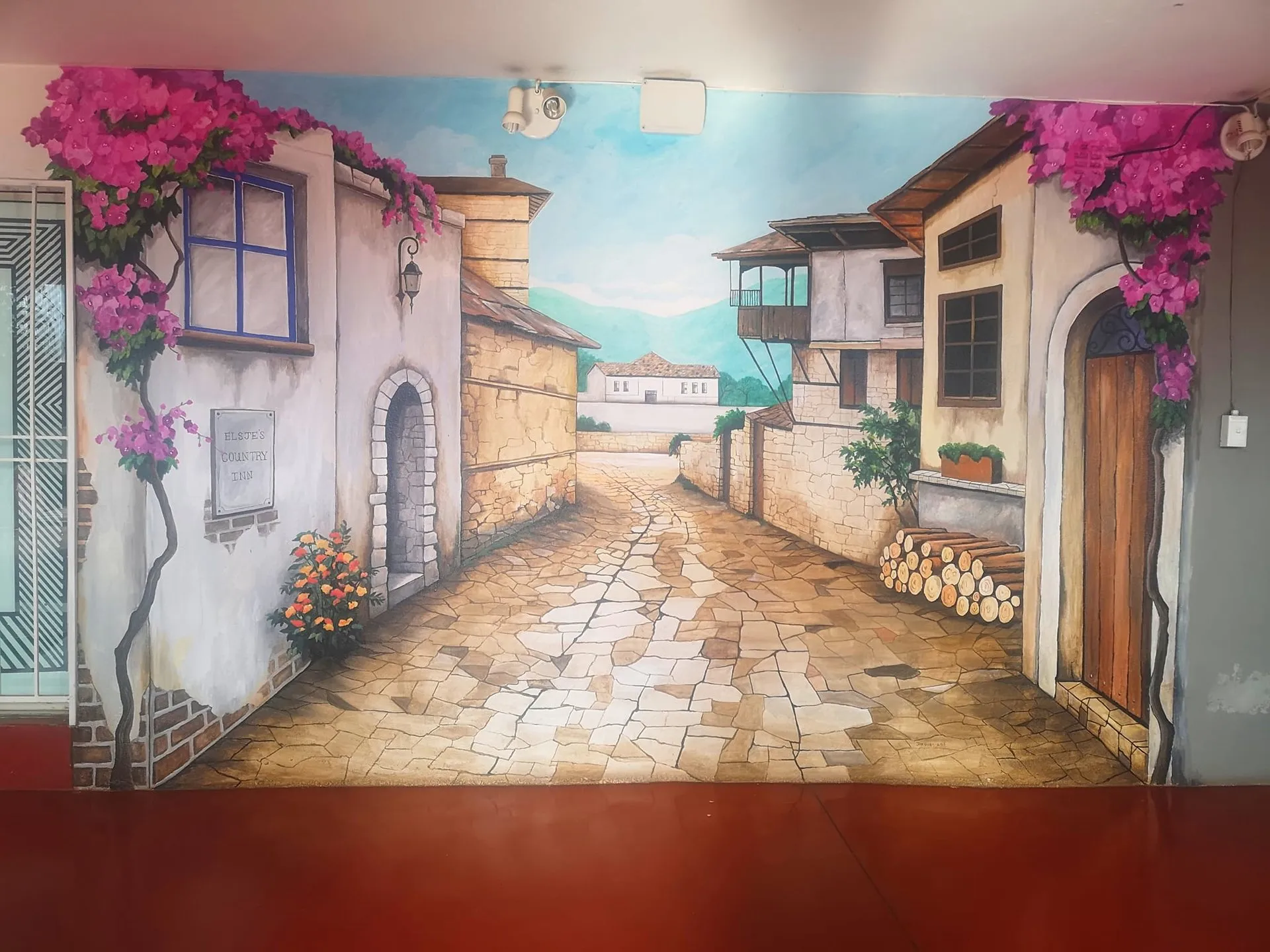 A painted mural of a village street, with the Elsjes Country Inn nameplate, inside the property