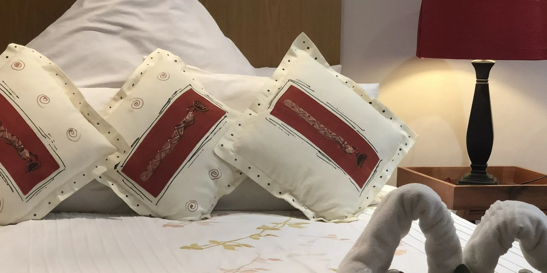 Close-up of embroidered cushions and a folded towel on a made-up bed